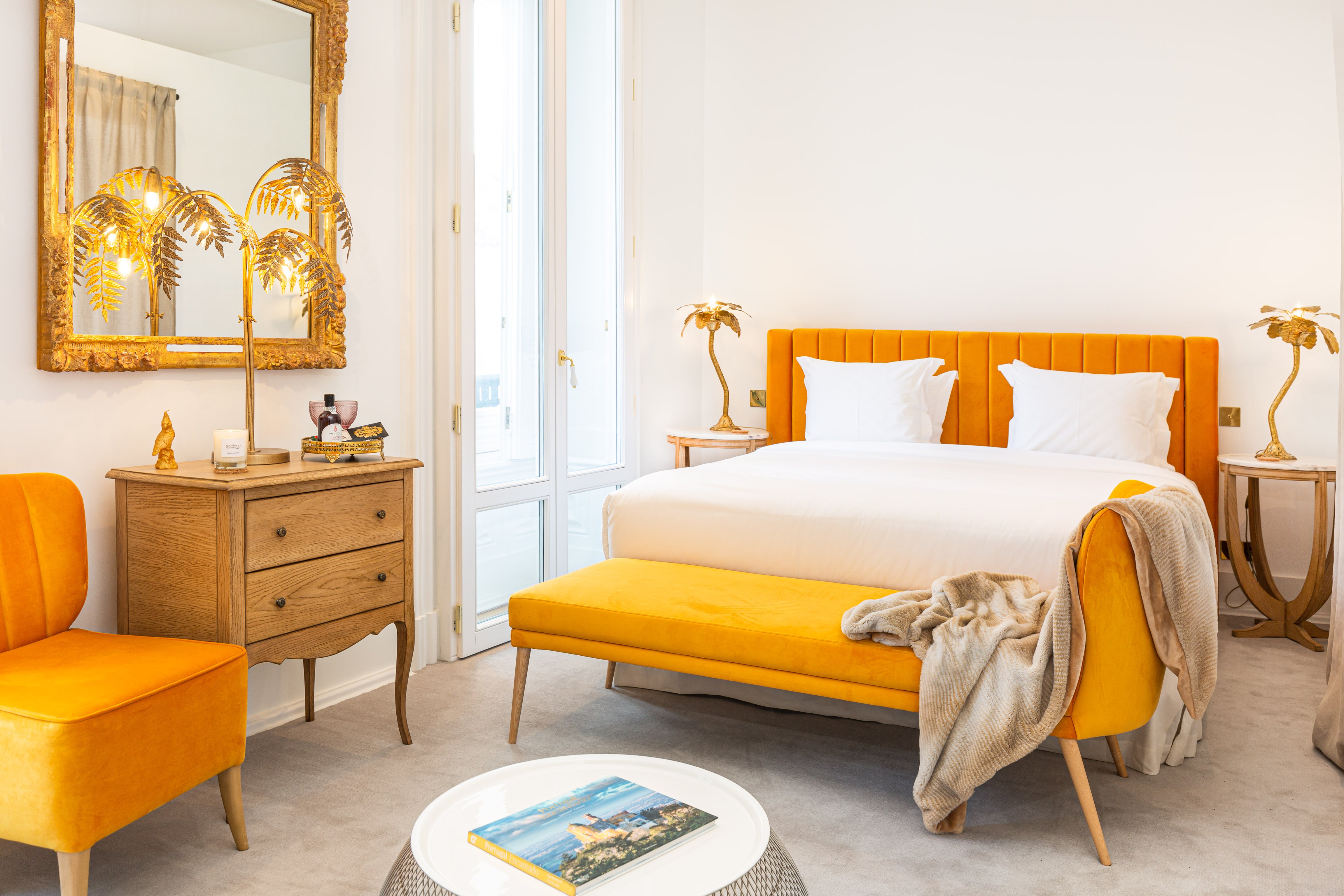 Bright guest room with an orange bed, matching bench, chandelier, and antique dresser