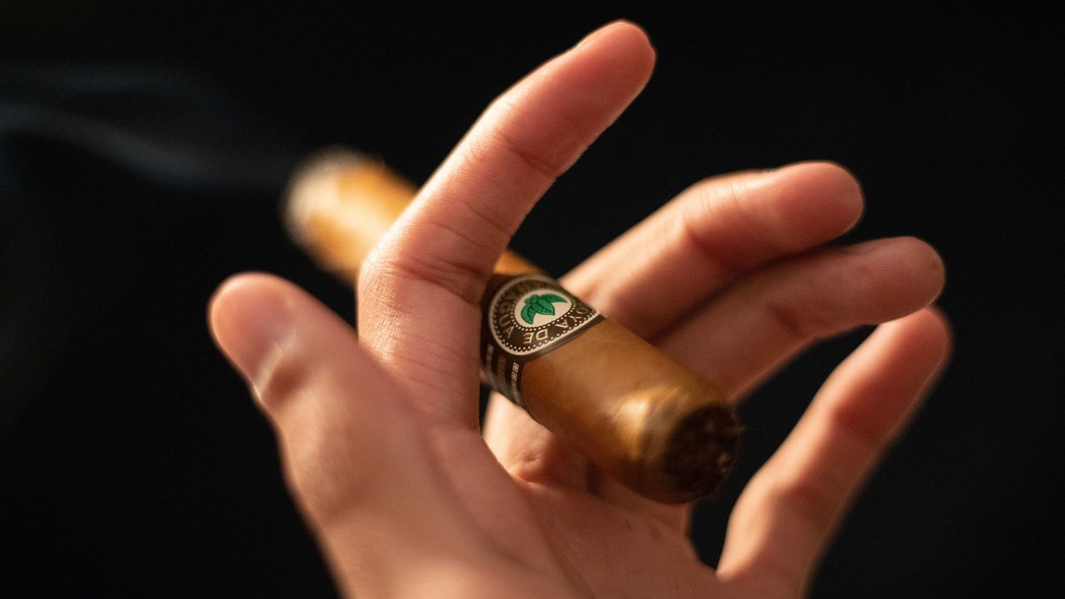 Close-up of a hand holding a lit cigar against a dark background