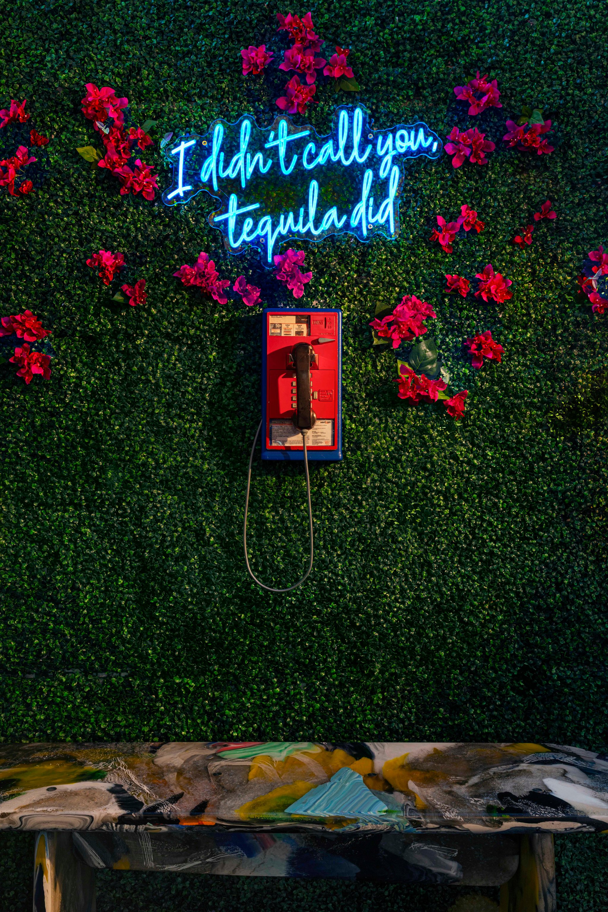 Neon lettering and a red telephone mounted on a flower-covered green wall