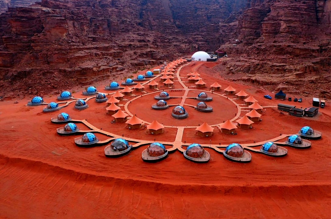 Glass-domed tents among red sandstone cliffs at Memories Aicha Luxury Camp