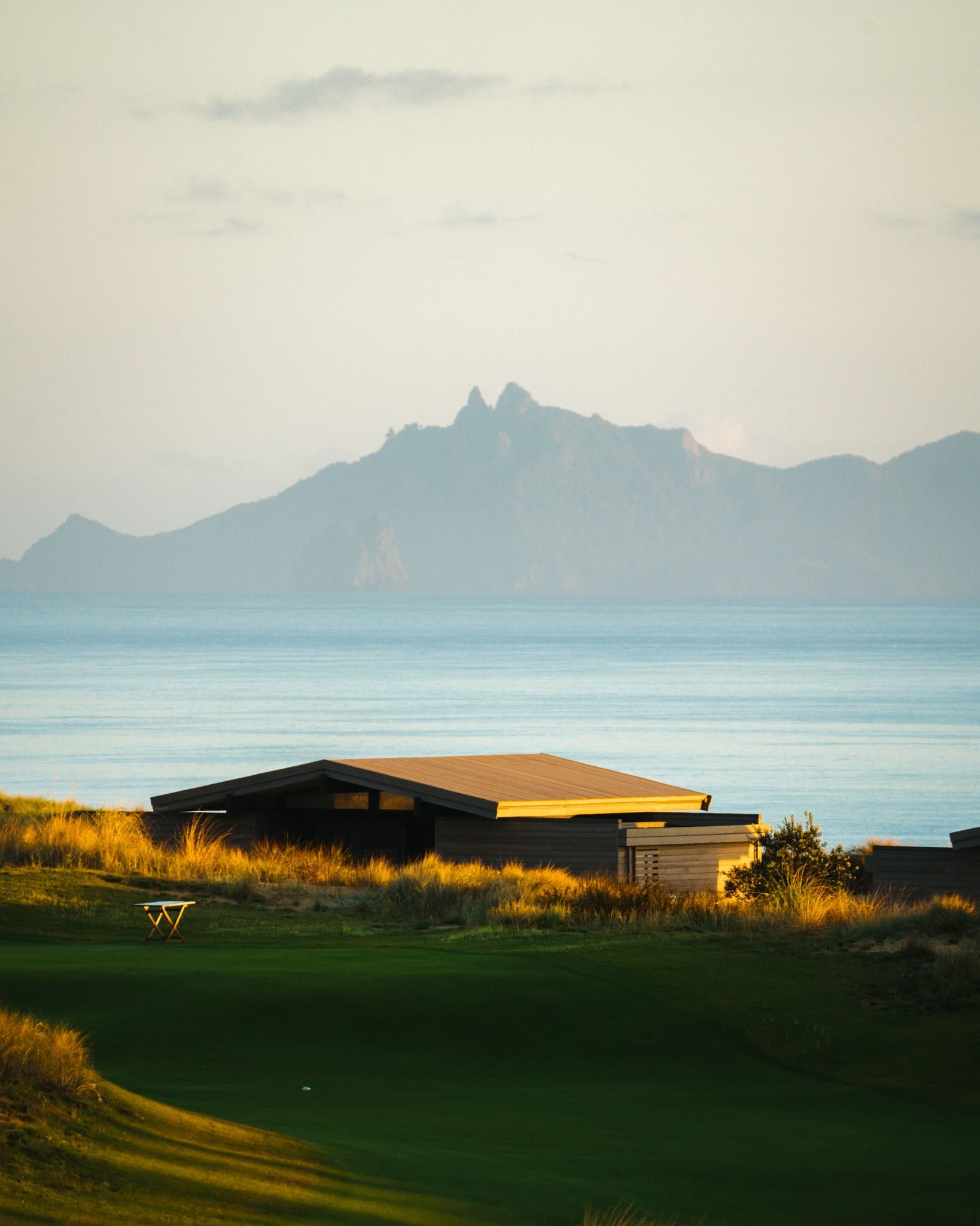 Low resort building among coastal grasses with water and distant hills beyond