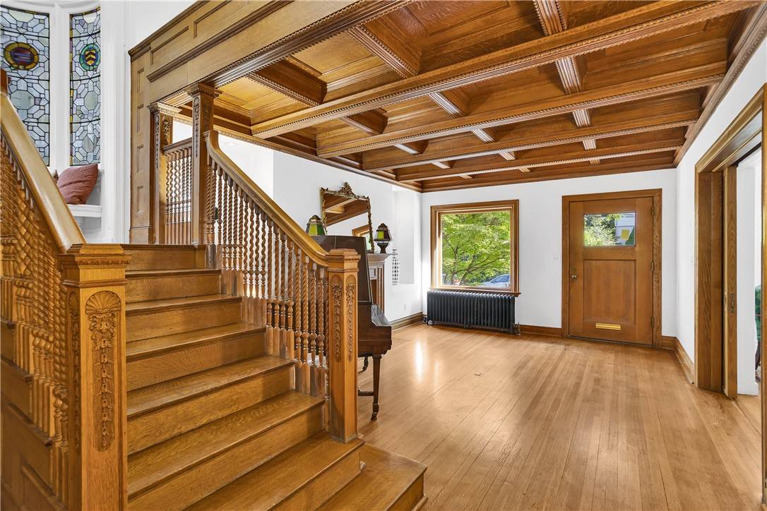 The oak staircase at 916 College Street under a coffered wood ceiling, with stained-glass windows on the landing