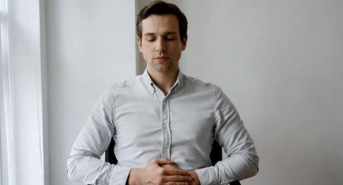 A man sitting calmly with one hand on his belly breathing slow