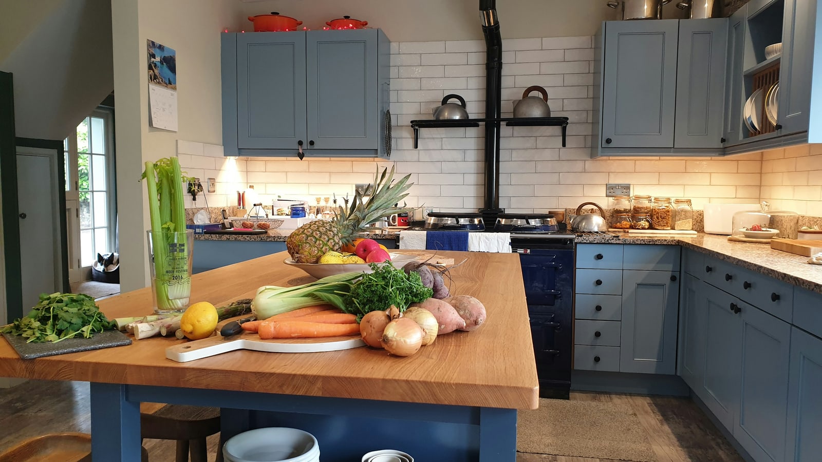 Blue Shaker-style kitchen cabinets around a wooden island with vegetables on the worktop.