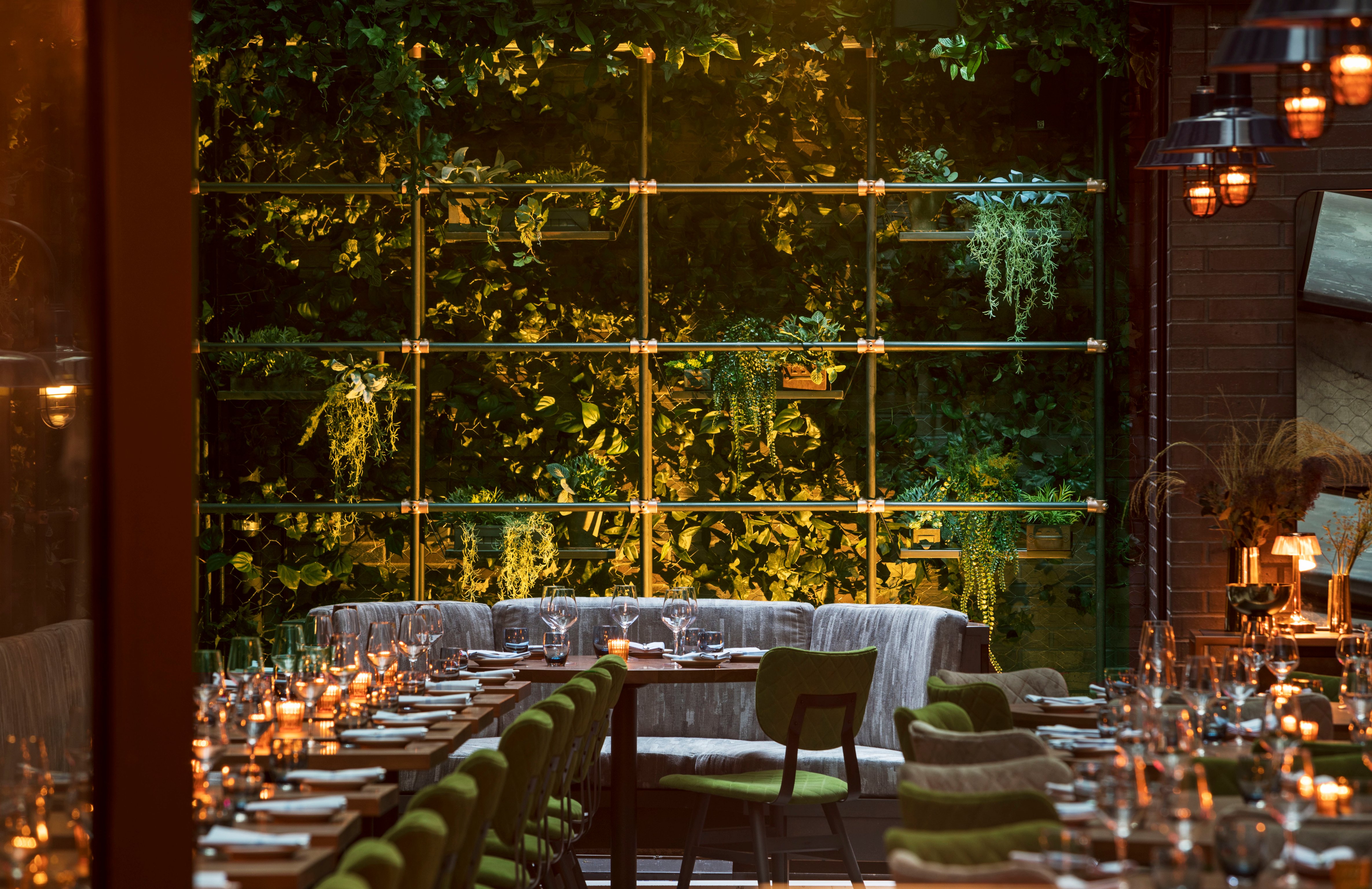 Dining terrace with greenery, candlelit tables, and upholstered seating
