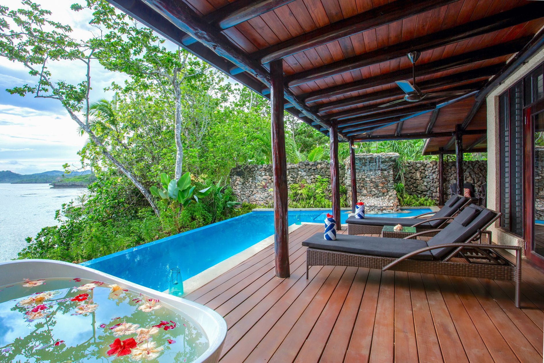 Massage beds and flower-filled bowl beside an ocean-facing pool