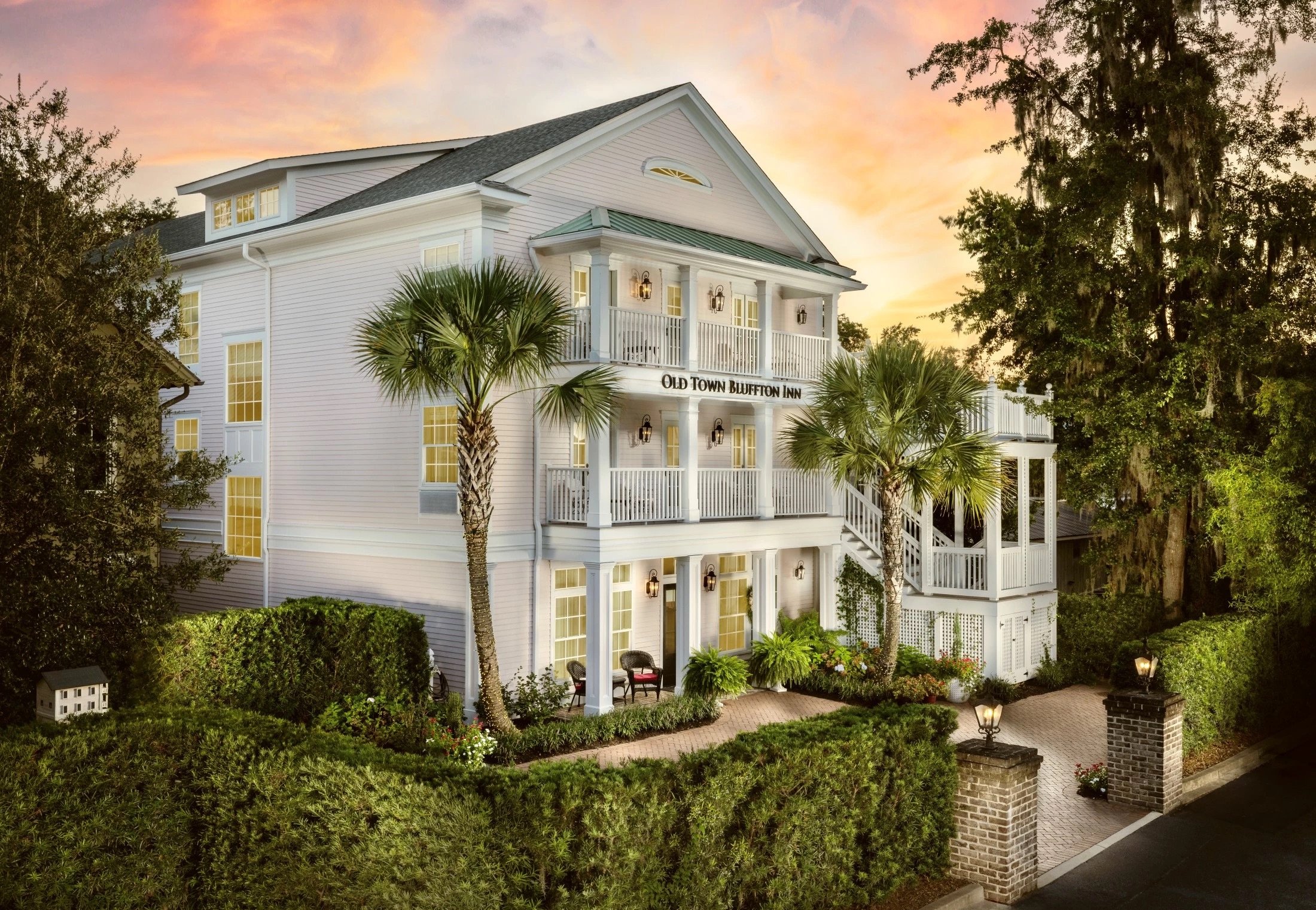 White inn with columned balconies and palm trees at sunset