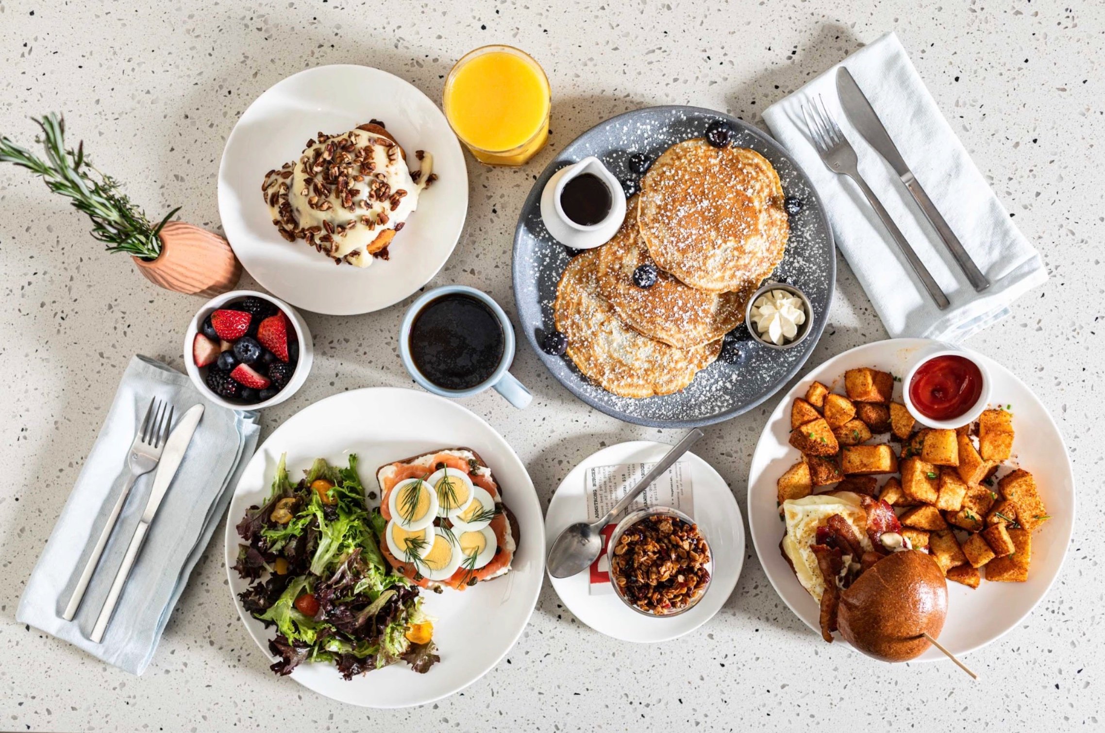 Overhead breakfast spread with pancakes, fruit, eggs, and pastries