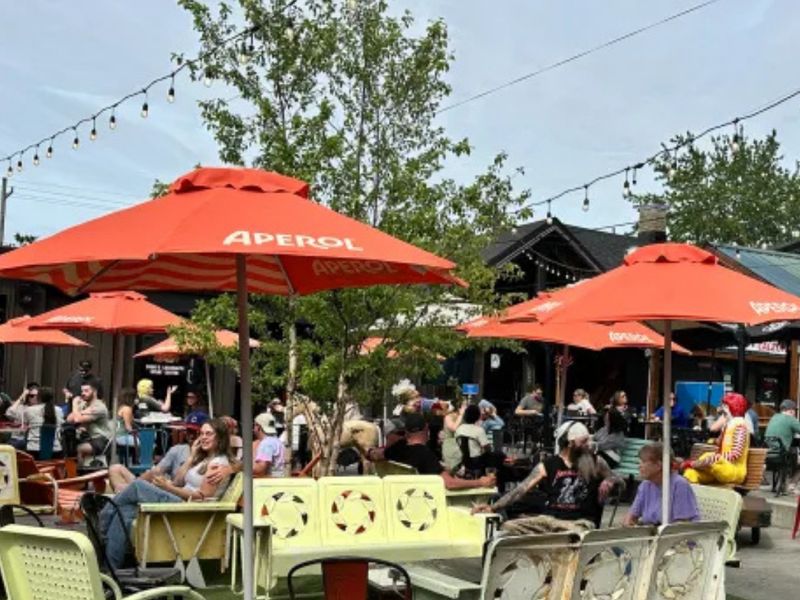 Turf patio with retro metal chairs and orange Aperol umbrellas at Hauck's Corner