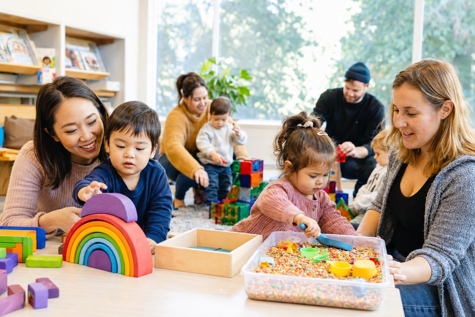 Toddlers and caregivers exploring colourful building and sensory activity stations in a library room