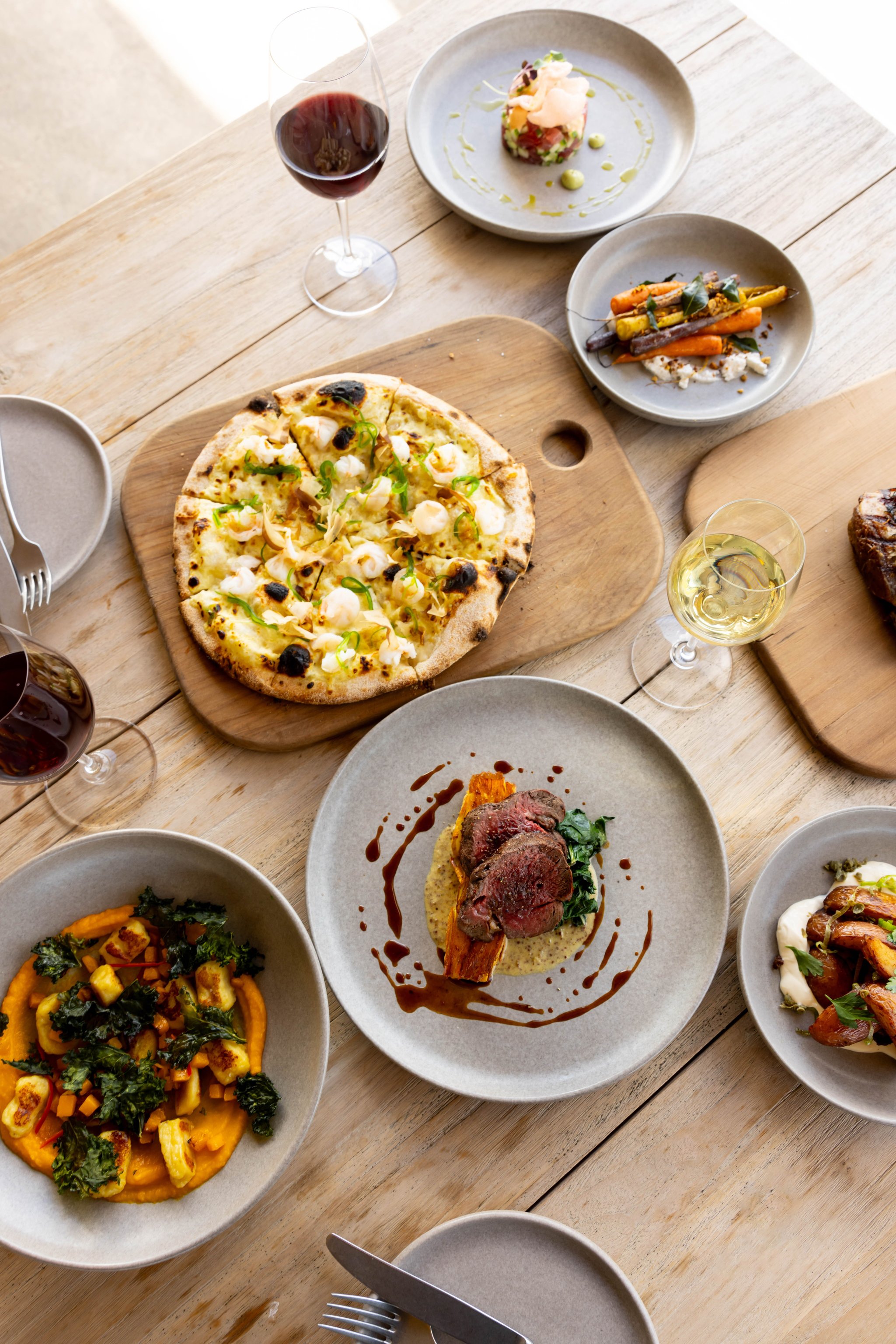 Table set with pizza, salads, plated dishes, and drinks
