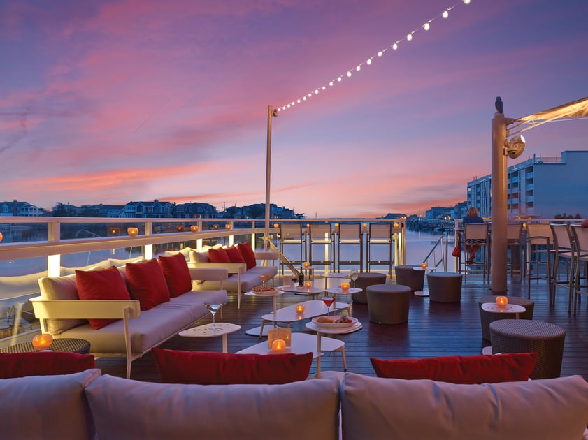 Waterfront rooftop seating beneath string lights at sunset
