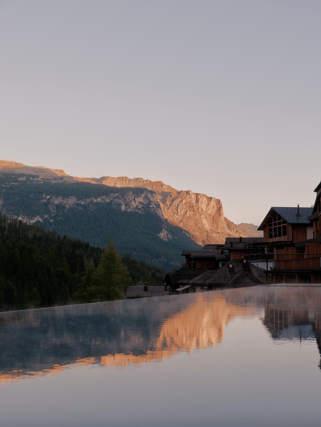 Reflecting pool and alpine lodge at dusk at Aman Rosa Alpina