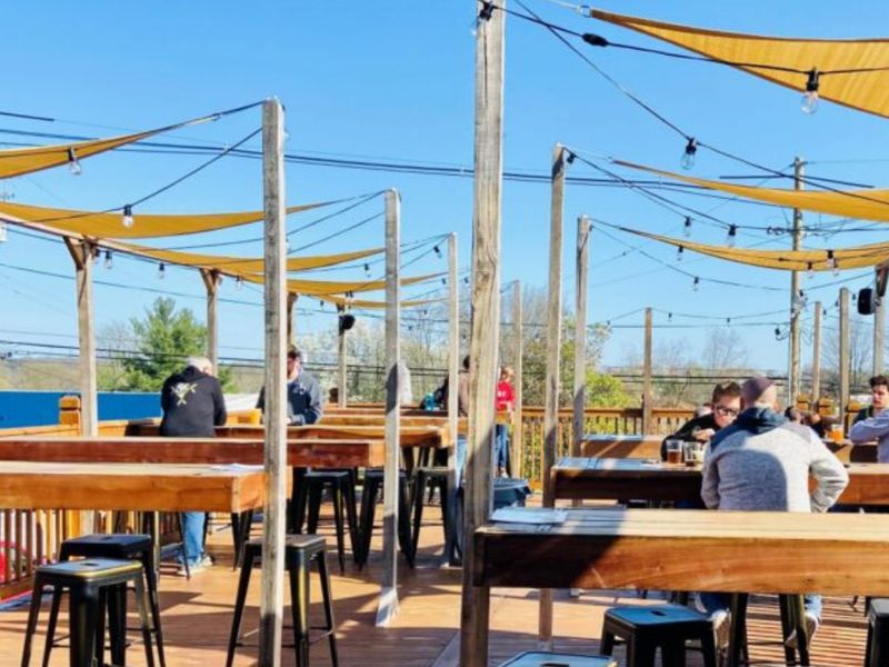Wooden deck with high-top tables under yellow sail shades at 3rd Turn