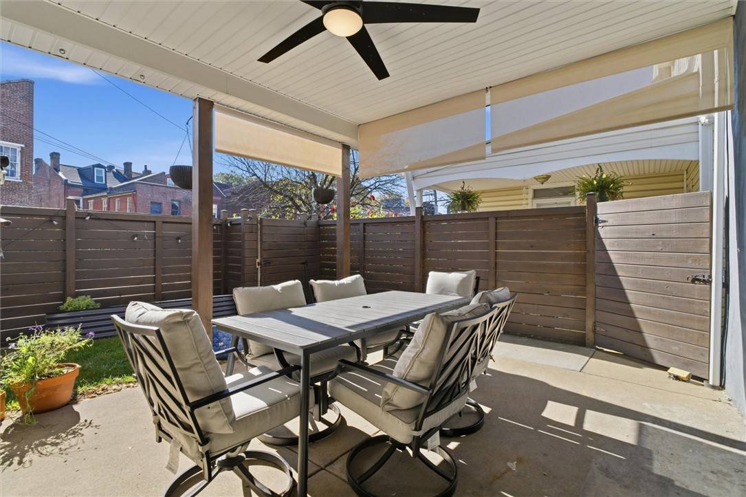 The covered back patio at 4916 Hatfield: a dining table for six under a ceiling fan, a wood privacy fence and a strip of lawn