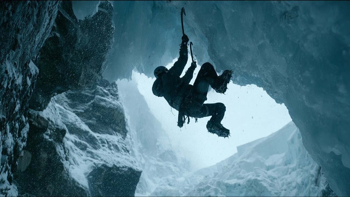 Silhouette of an ice climber hanging from ice axes beneath a frozen overhang