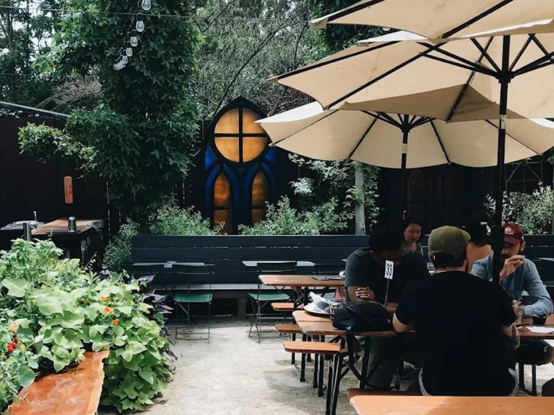 Gravel beer garden with umbrellas behind the stained-glass window at Holy Grale