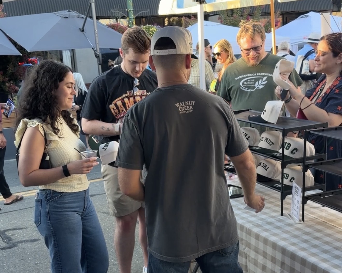 Shoppers trying on The Nut hats at the Walnut Creek Spotlight booth at the Locust Street Festival.