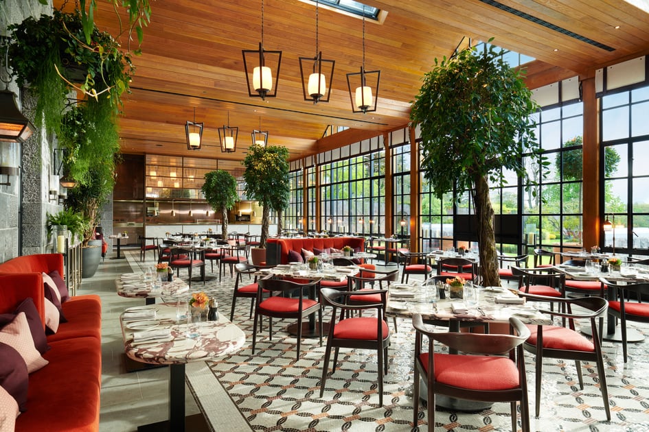 Glass-roofed dining room with red chairs and greenery at Adare Manor
