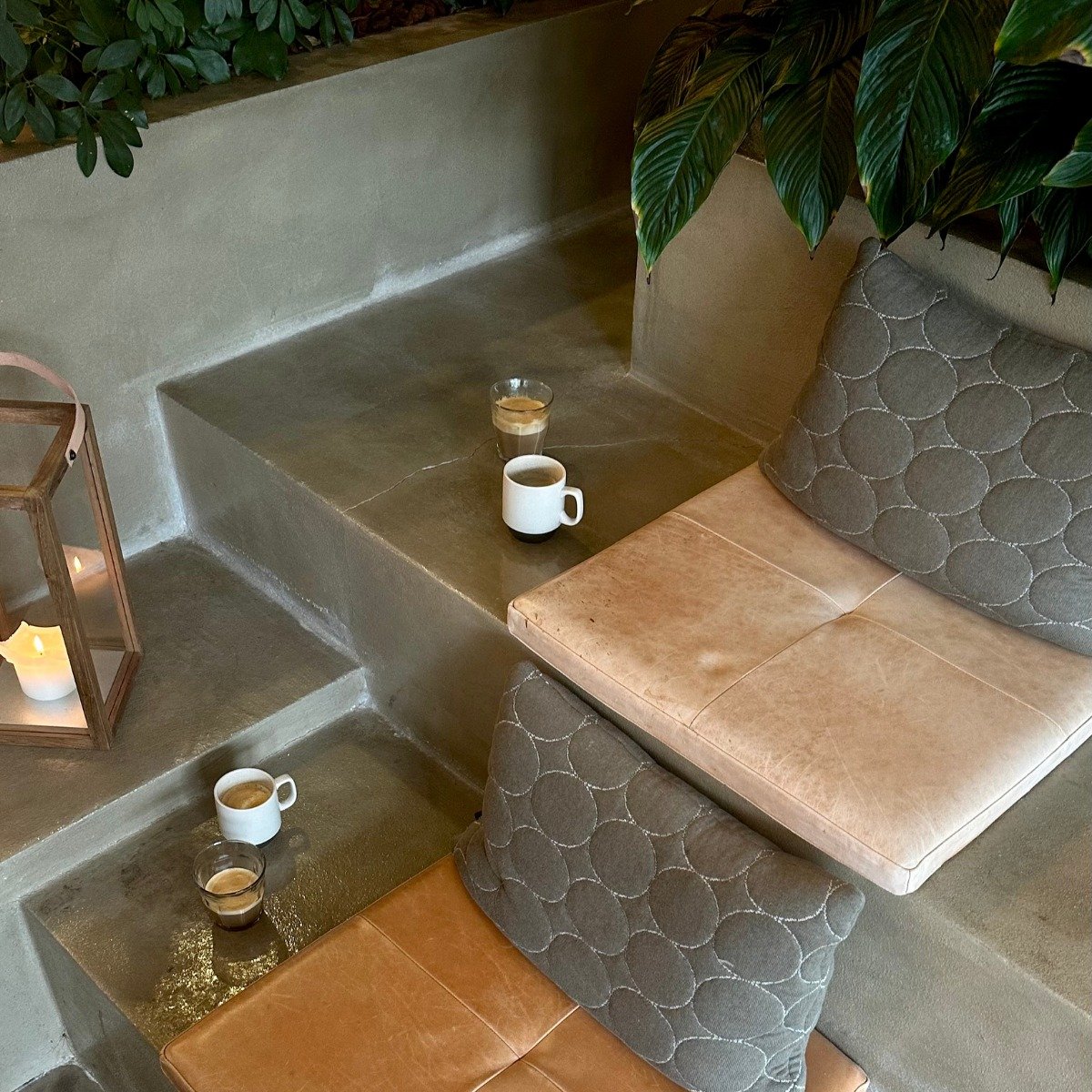 Tiered concrete seating nook with tan cushions, hexagonal tile, candles, and cups
