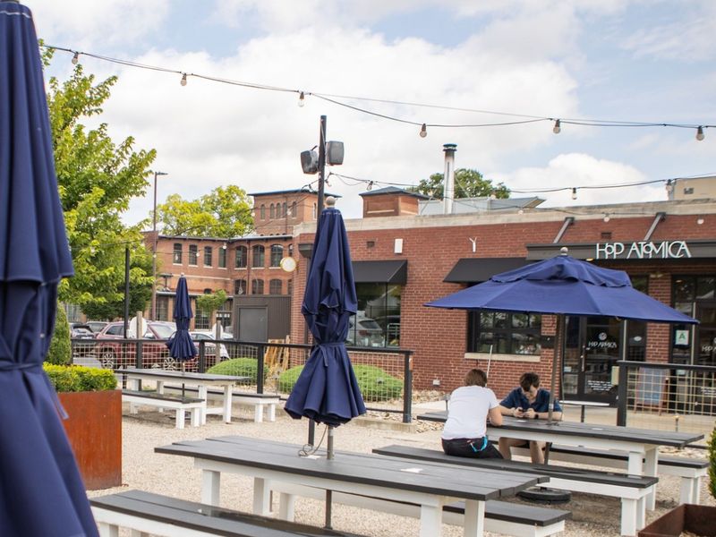 Gravel patio with picnic tables and blue umbrellas at Hop Atomica