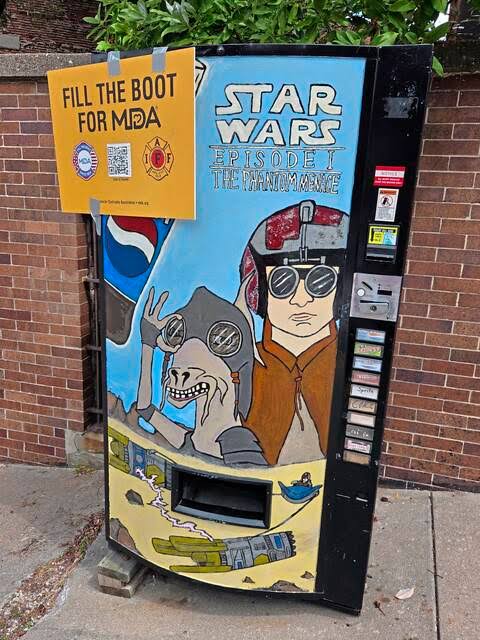 The hand-painted replica Star Wars vending machine propped on blocks against the brick wall on Virginia Avenue, its crude Phantom Menace artwork and a taped-on Fill the Boot for MDA sign