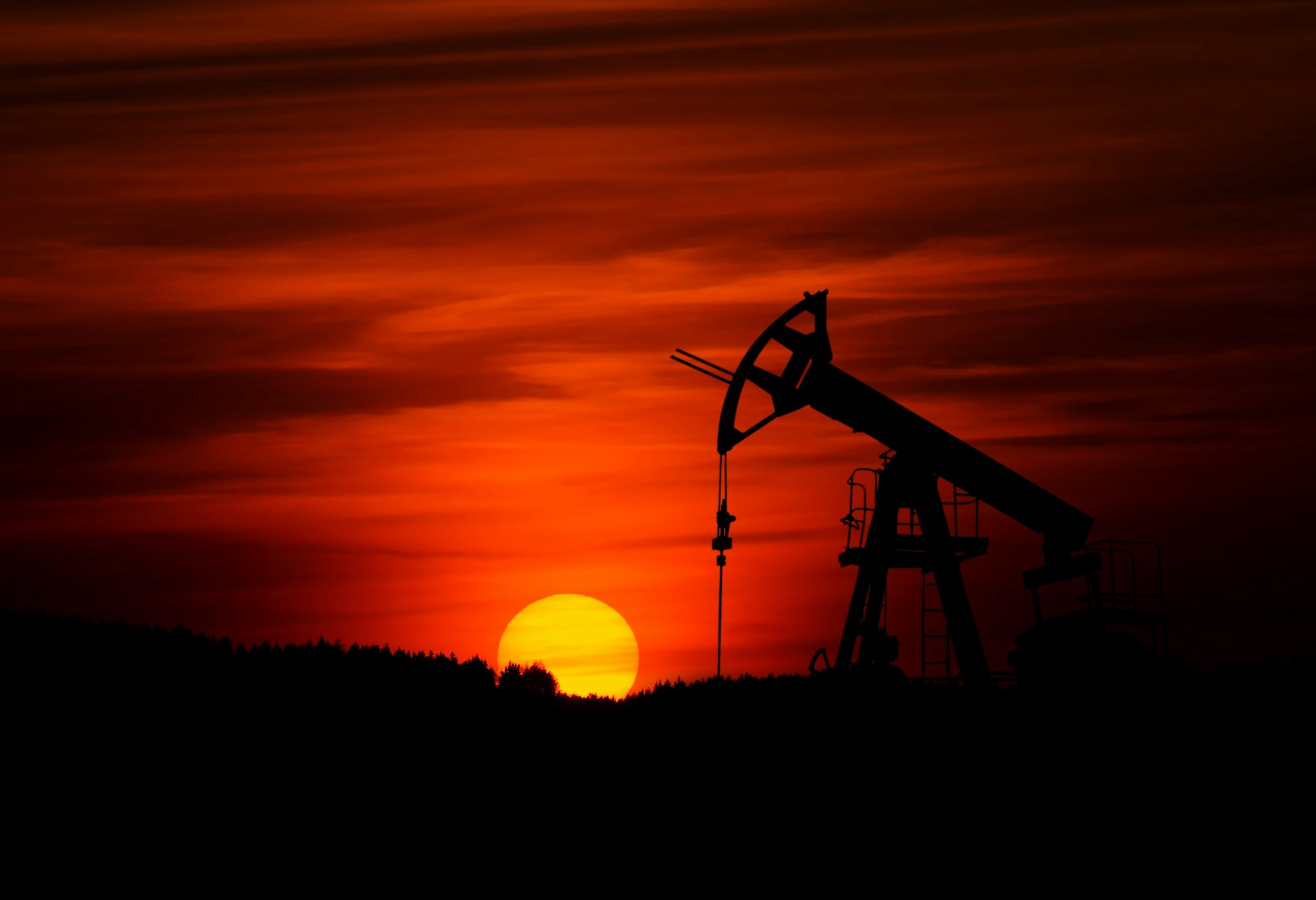 Oil pump jack silhouetted against a red sunset sky