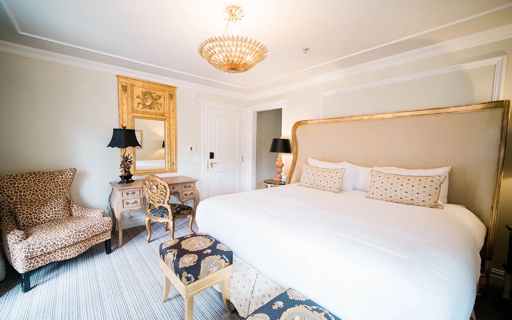Guest room with a cream upholstered bed, chandelier, and patterned chairs