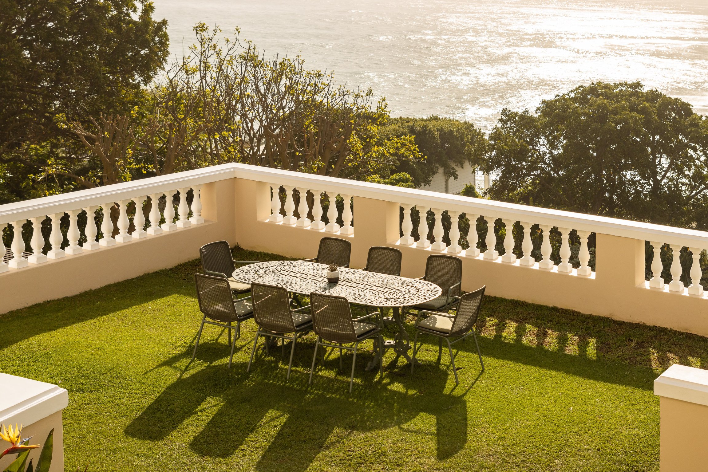 Ocean-view lawn terrace with a white balustrade and outdoor dining table