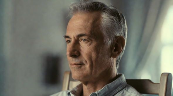 A man seated upright gently turning his head to look over his shoulder