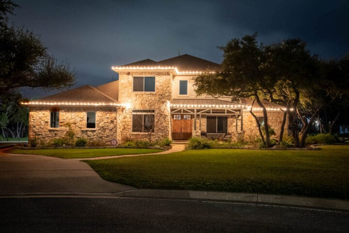 Stone home lit with white holiday lights along the roofline