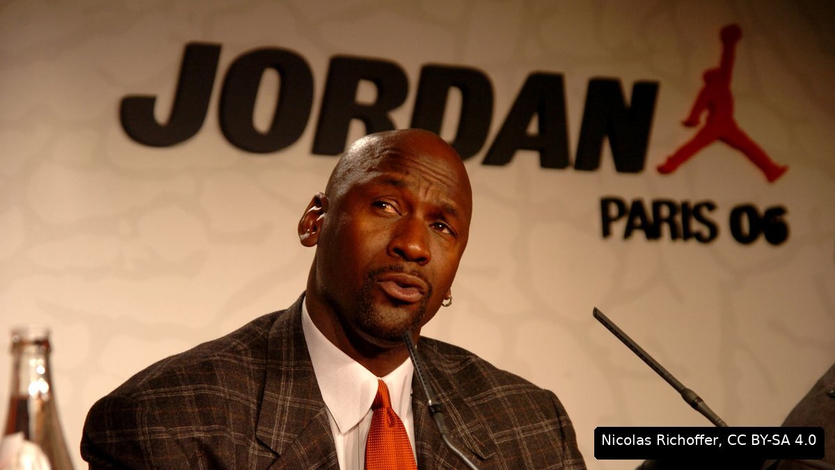 Michael Jordan speaking at a press conference in front of a Jordan brand backdrop