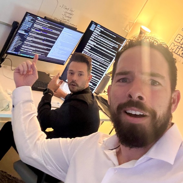 Adam and a friend at his desk, pointing at the monitors
