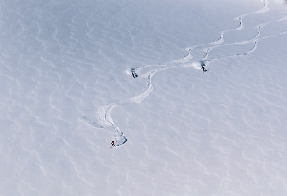 Skiers carving tracks through an open snow-covered mountain slope
