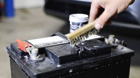 Car battery terminals being cleaned with a wire brush