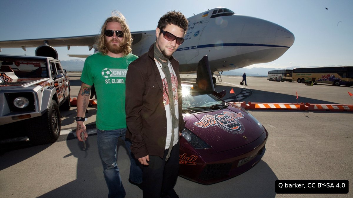 Ryan Dunn and Bam Margera on an airport runway in front of a cargo plane and a Lamborghini