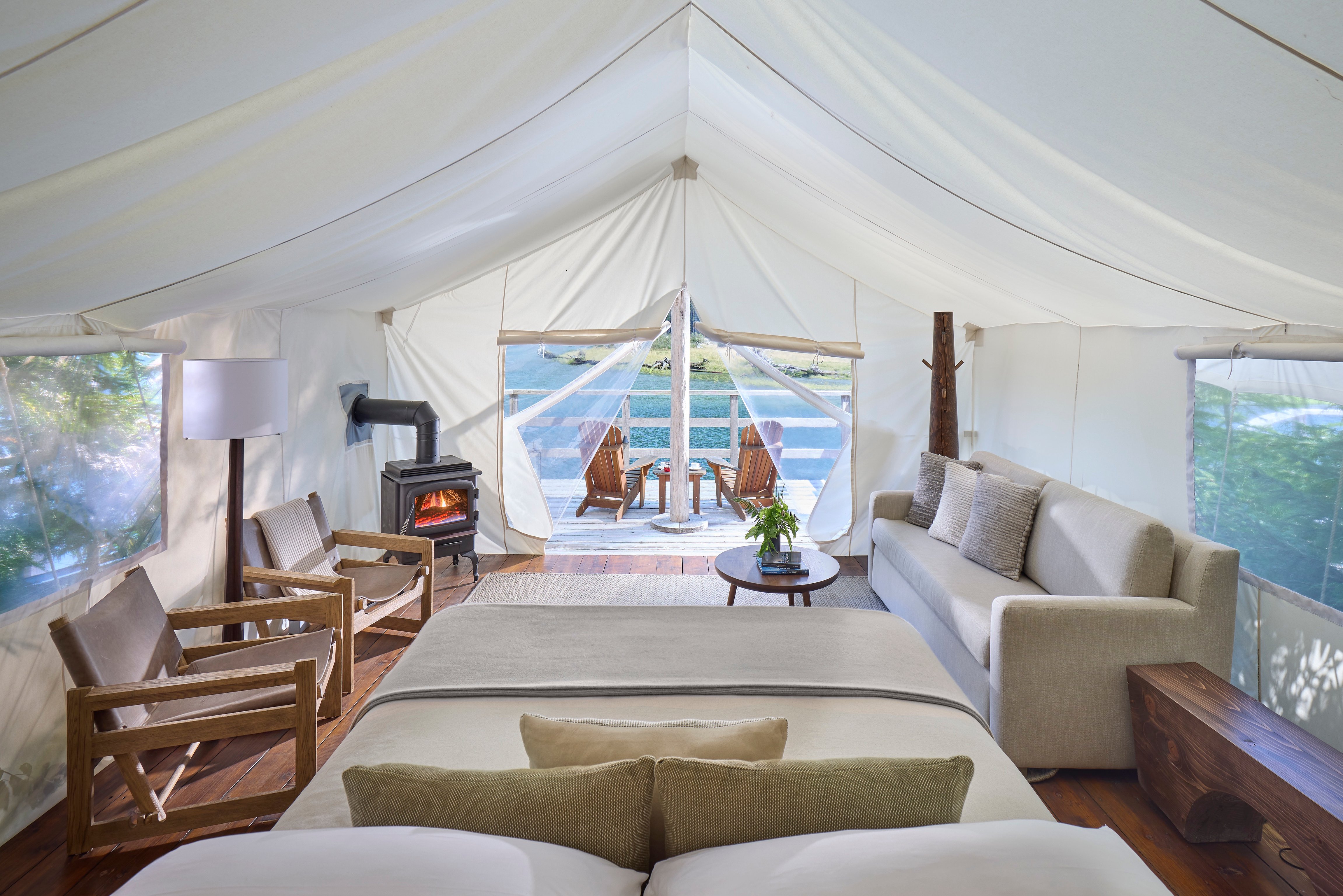 Luxury canvas tent with white canopy, seating area, wood stove, and deck