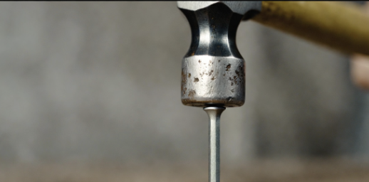 Close up of a hammer tapping the point of a nail to blunt it