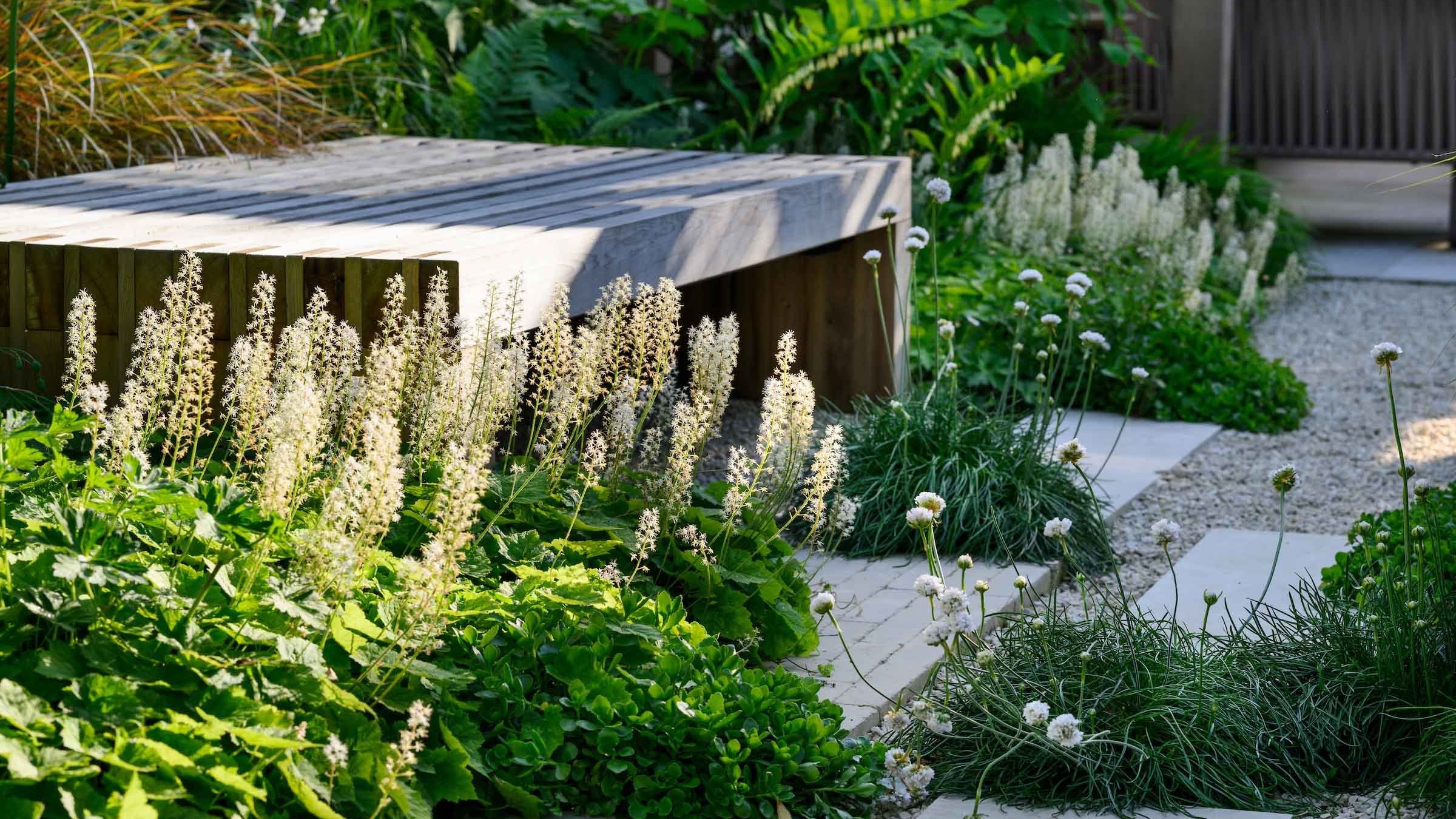 A timber garden bench surrounded by planting beside a gravel path in Putney.