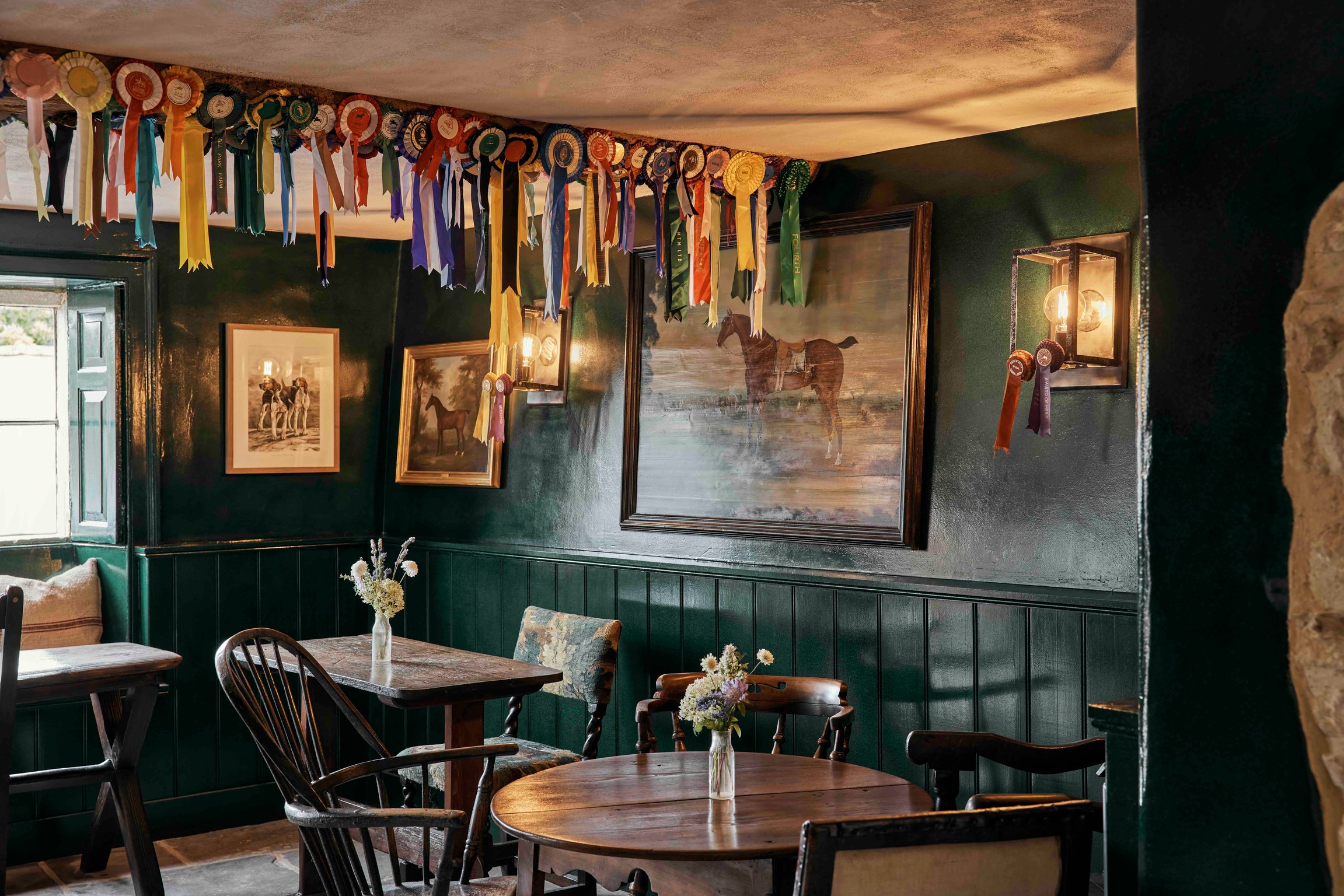 Green-paneled pub room decorated with rosettes at The Fox at Oddington