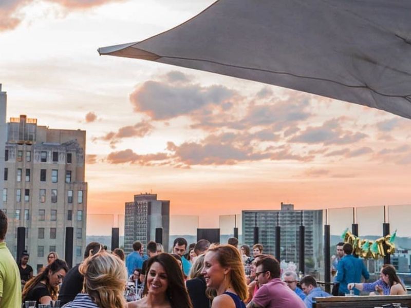 Crowded rooftop with a fire table and skyline sunset at 8UP