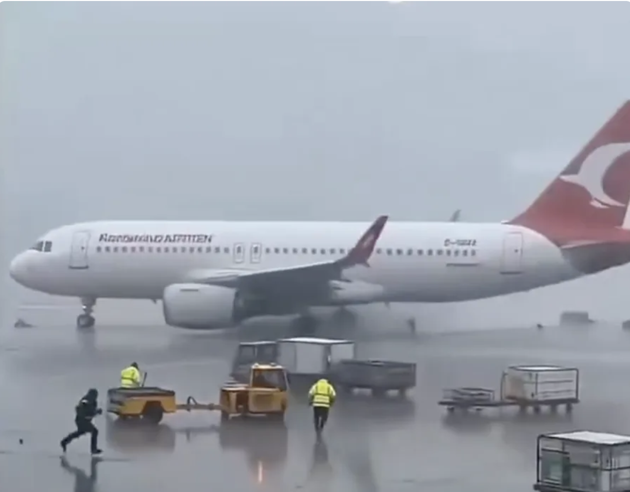 An airplane spinning uncontrollably across a rain-soaked runway as ground workers scatter, several appearing to be struck before getting up unharmed