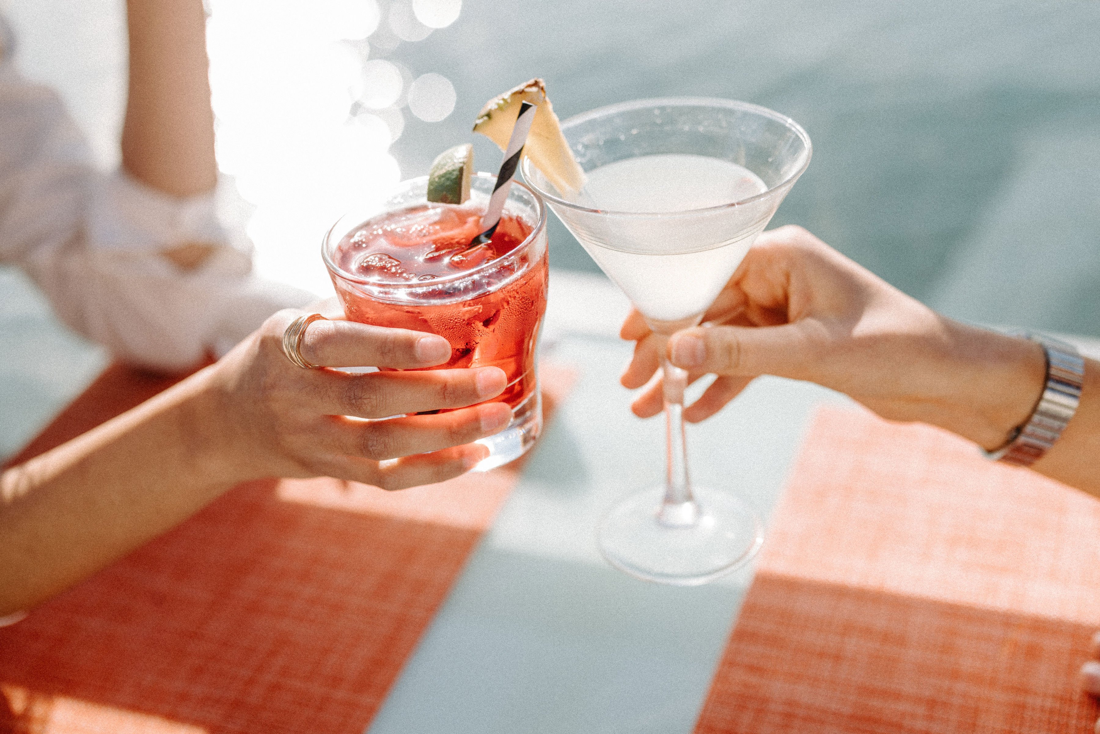Two guests toasting colorful cocktails beside the water