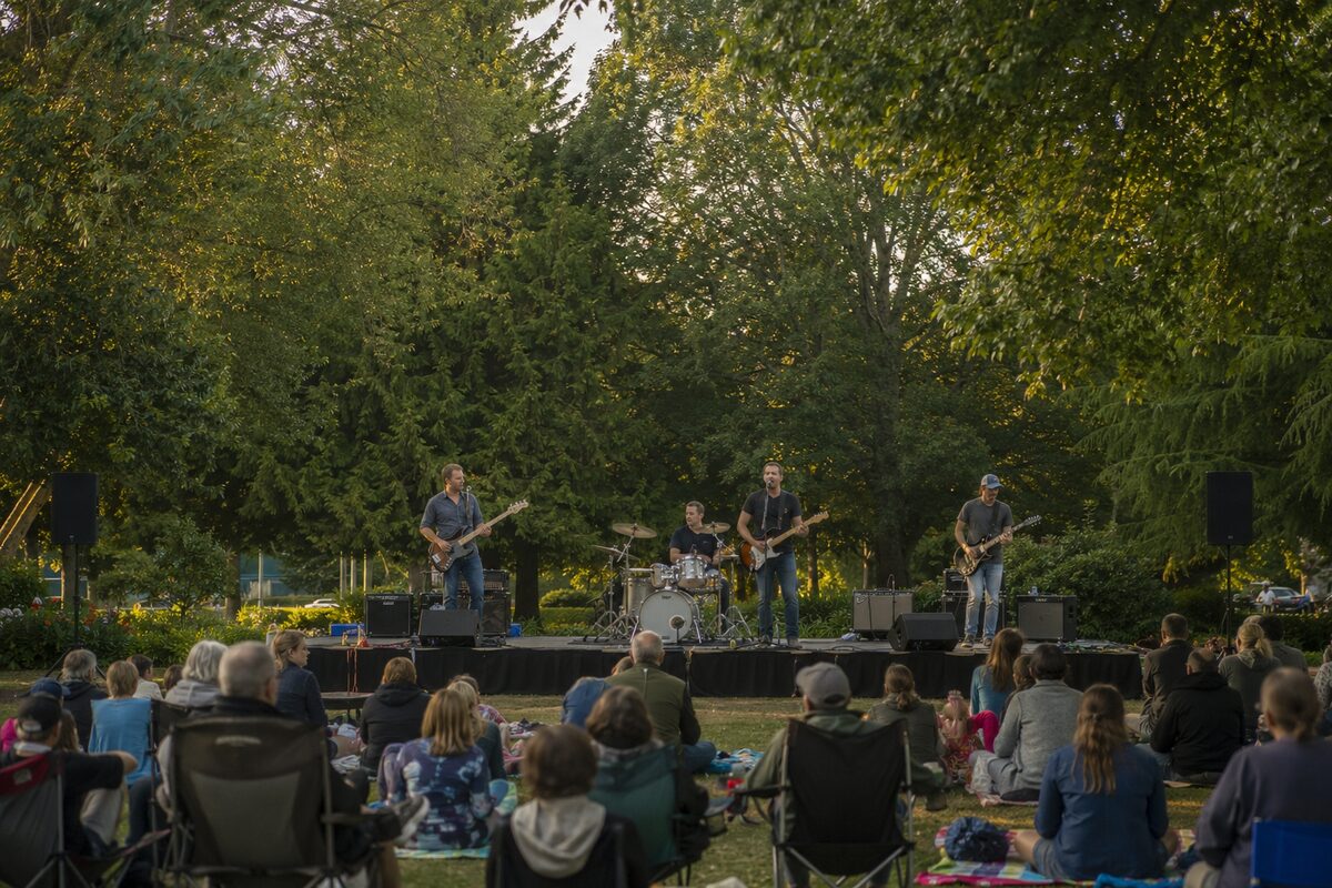 Four-piece rock band playing an outdoor evening concert in a leafy community park