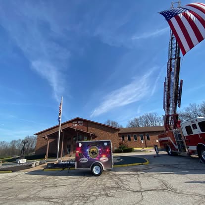 Large American flag hanging over a fire truck and BackStoppers of Jefferson County trailer