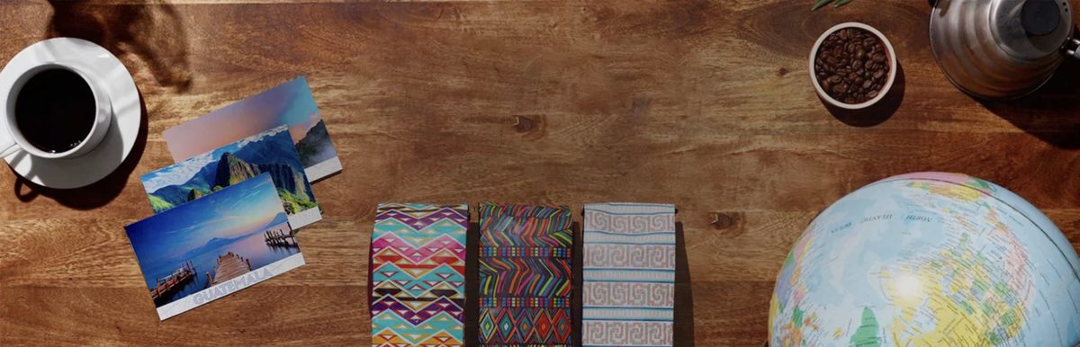 Atlas Coffee Club coffee bags, postcards from Guatemala and Peru, a globe, and a cup of coffee on a wooden table