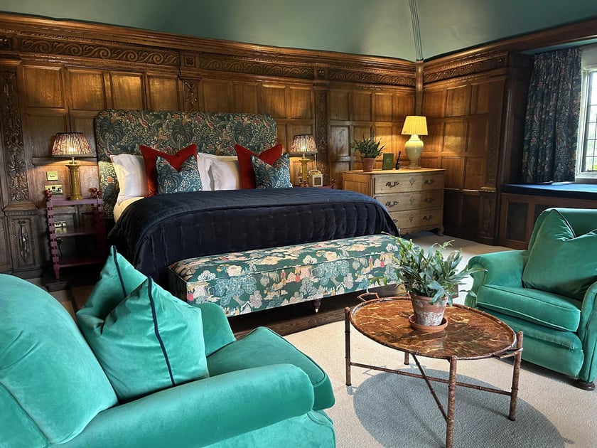 Wood-paneled guest room with green seating and a period bed