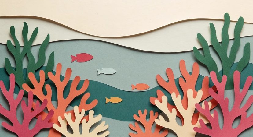 A paper cutout coral reef in green, coral pink and cream with small fish swimming above it