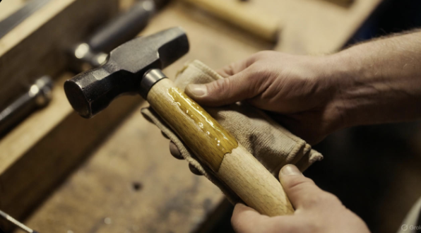Hands applying oil to a wooden tool handle with a cloth