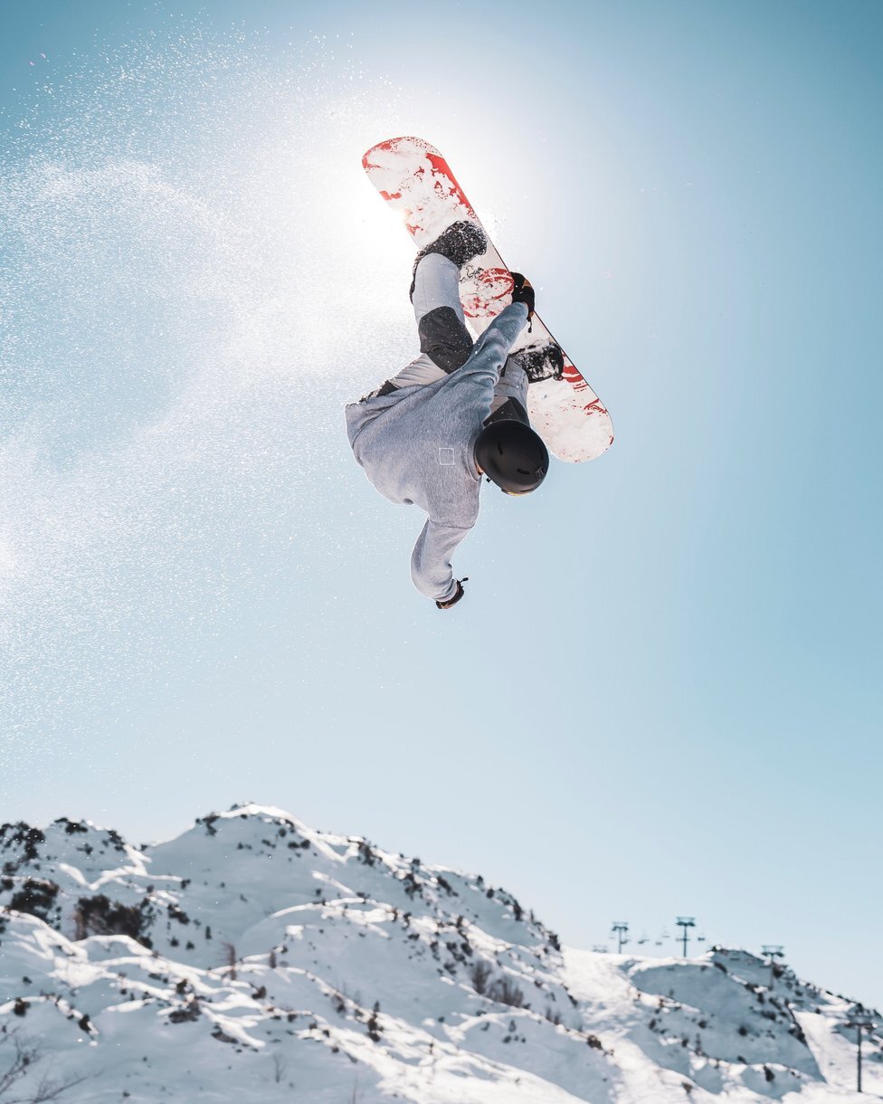Snowboarder flipping upside down mid-air above snowy mountains